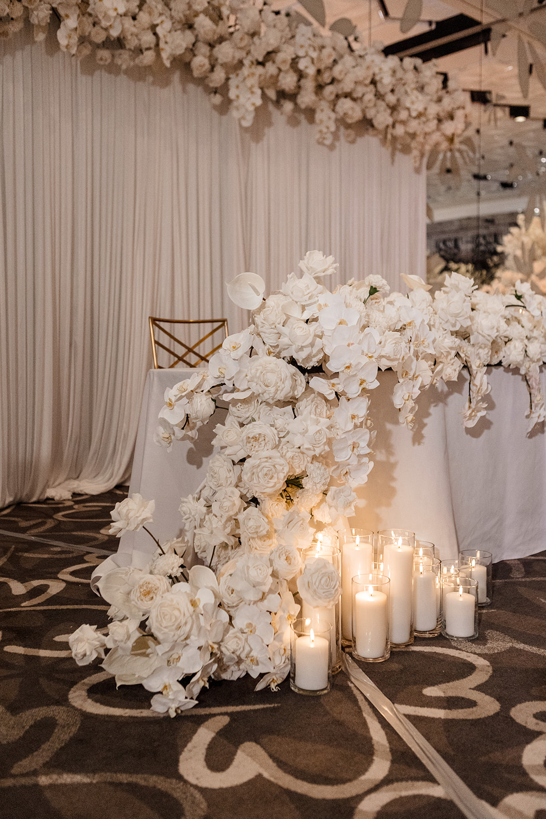Faux orchid and rose floral table runner in all white with cylinder pillar candles at indoor reception space in Brisbane.