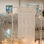 Soft linen fabric seating chart signage hung on a white display stand and styled with premium faux florals and pillar candles in glass holders.